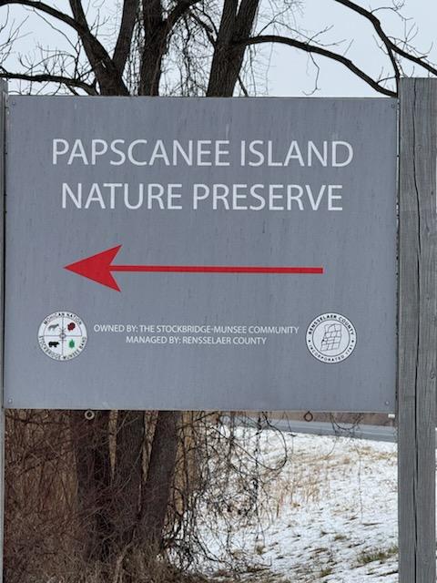 A sign read "Papscanee Island Nature Preserve" above a red left-pointing arrow. On the bottom fo the sign is the official seal fo the Stockbridge-Mundsee Band of Mohicans.